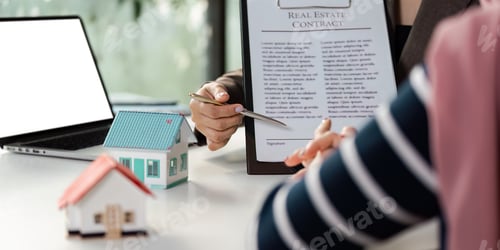 Preview: Real estate agent presenting a contract to a client with model houses on the table.