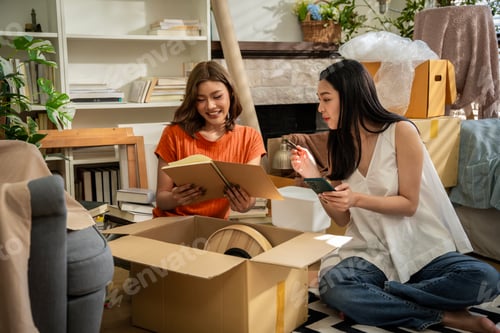 Preview: Two women sitting on a checkered rug in a room with boxes and books