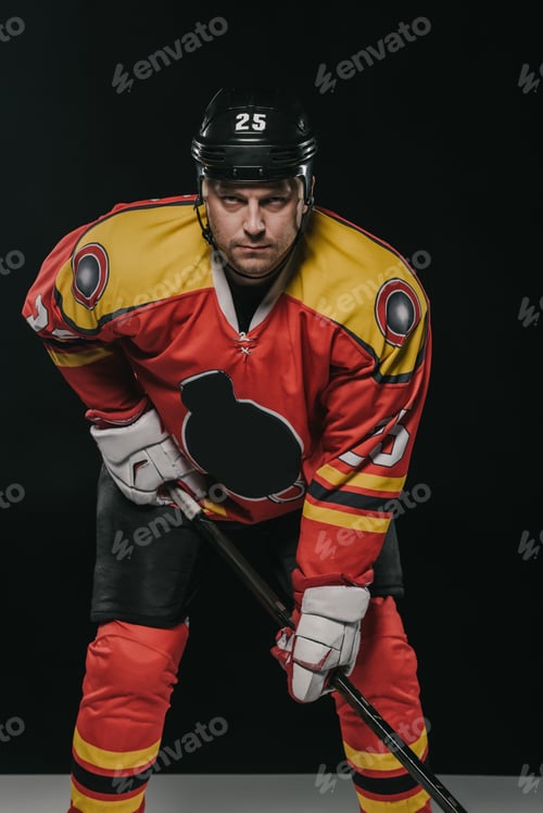Preview: professional ice hockey player holding hockey stick and looking at camera on black