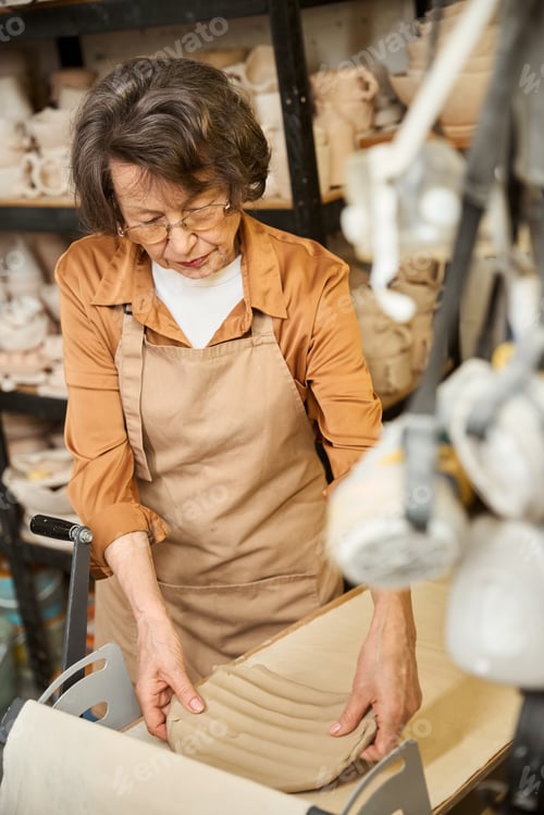 Preview: Lady in a work apron rolls out a layer of clay