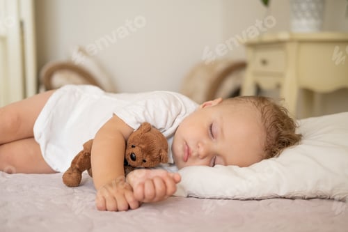 Preview: funny baby boy sleeping on bed at home. child hugging teddy bear