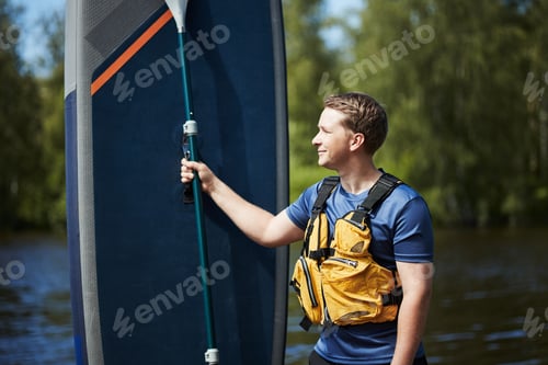 Preview: Caucasian Young Adult Man Holding Paddleboard While Standing near Lake