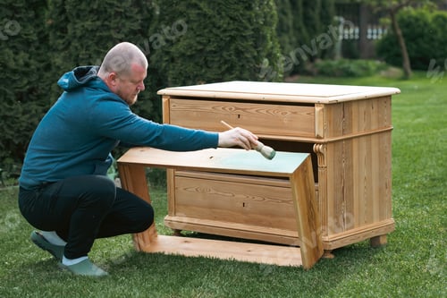 Preview: Man painting a wooden furniture while sitting with hir dog in the garden. DIY concept.