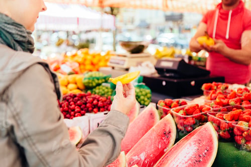 Preview: Midsection of woman holding slice of mango at fruit stall