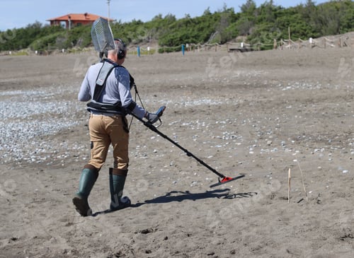 Preview: Man holding a metal detector while standing on a sandy beach