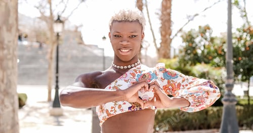 Preview: Cheerful black queer person showing heart gesture and smiling on street