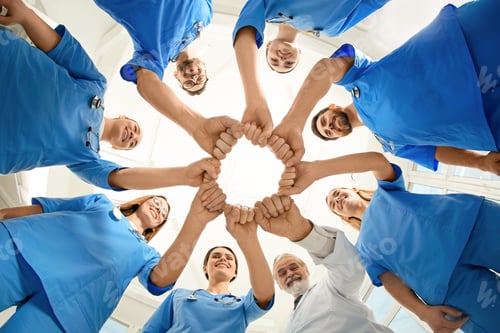 Preview: Doctor and interns holding fists together indoors, bottom view