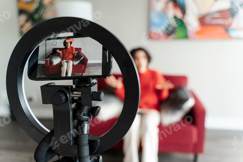 Preview: Curly positive lady blogger recording video blog on smartphone camera at home