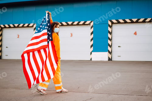 Preview: African American woman with medical face mask posing with american flag. Covid-2019.