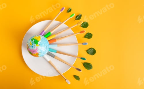 Preview: Colored Bamboo Toothbrushes are located around the small planet Earth on a white yellow background