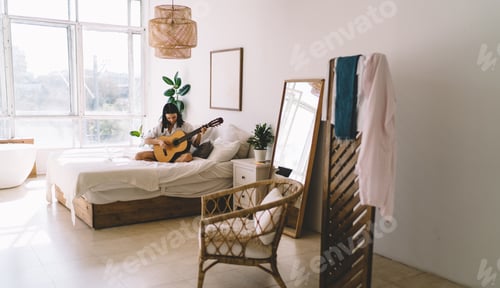 Preview: Young woman with netbook enjoying hobby with musical instrument relaxing on bed