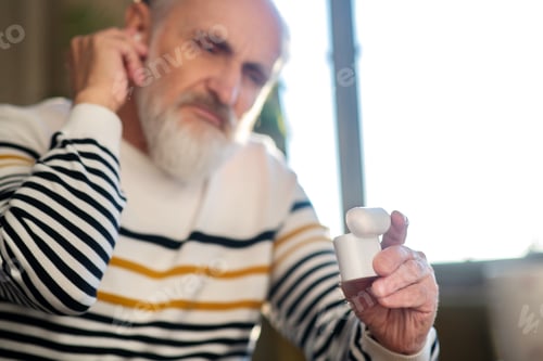 Preview: Grey-haired bearded man in striped sweater attaching wireless earphone
