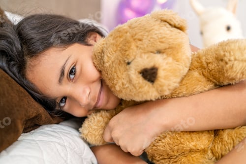 Preview: Smiling girl hugging teddy bear while lying in bed before sleeping