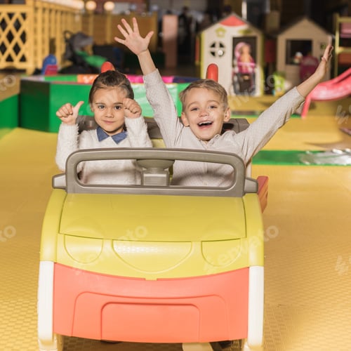 Preview: adorable happy siblings sitting in toy car and smiling at camera in entertainment center