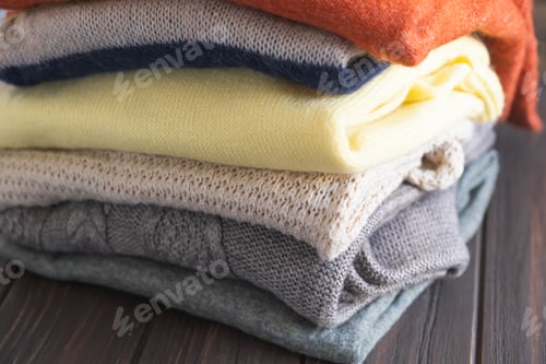 Preview: Cozy sweaters in autumn colors on brown wooden background.