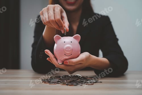 Preview: Asian female finance businessman putting coins into a piggy bank To save money and plan for it after