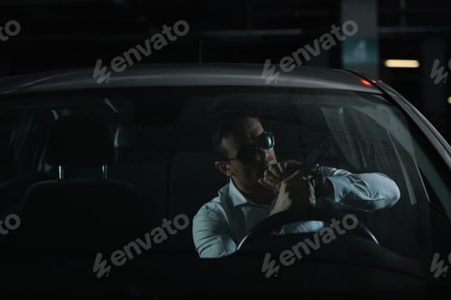 Preview: serious male undercover agent in sunglasses charging gun in car