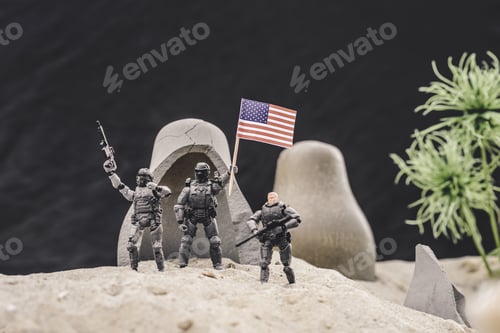 Preview: selective focus of toy soldiers with guns and american flag standing near caves on sand dune