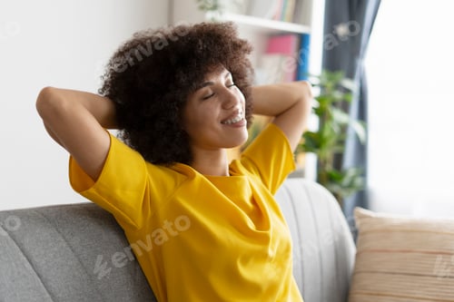 Preview: Smiling African American woman relaxing on sofa: embracing peace and comfort at home