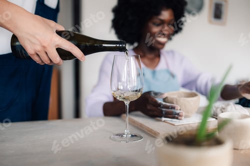 Preview: Close up hand pouring wine into a wineglass on pottery class.
