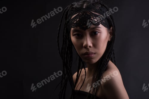 Preview: Young Asian Woman With Ethnic Braids At Studio Over Dark Background