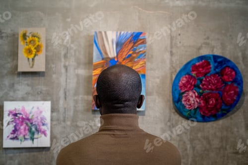 Preview: Rear view of young African man looking at paintings on wall