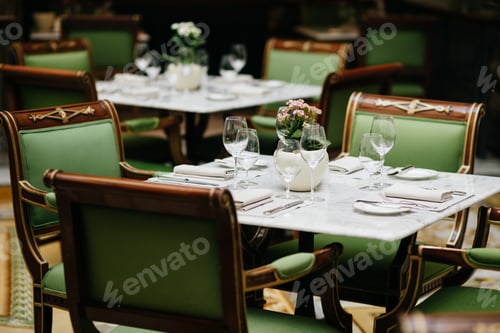Preview: Table served with luxury glasses, cutlery, flowers, green chairs around in cozy restaurant.