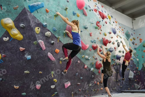 Preview: Group of three young sportswomen in activewear exercising on climbing wall