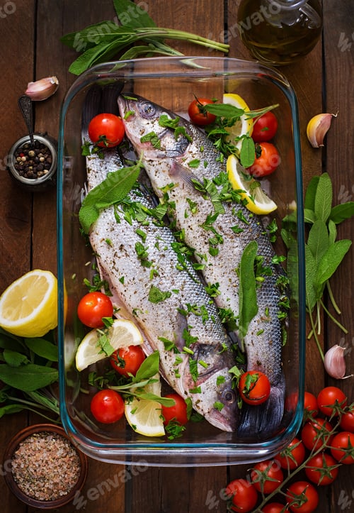 Preview: Two raw seabass in a baking dish with spices on an old wooden background. Top view