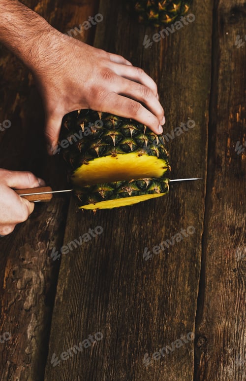 Person Cuts Pineapple on Rustic Wooden Surface