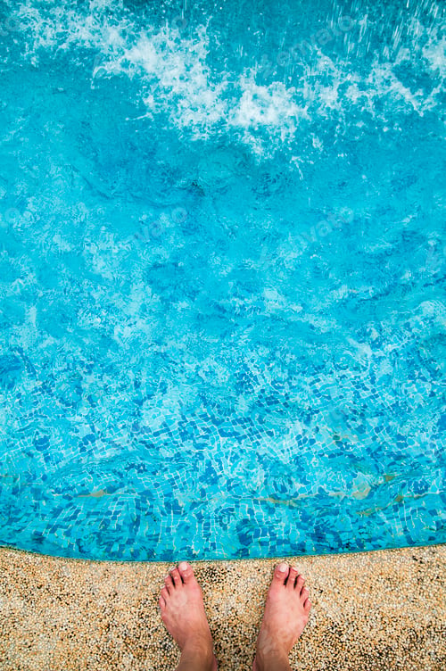 Preview: Top view of human feet standing on edge of blue water swimming pool