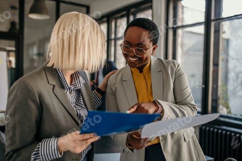 Preview: Businesswomen discussing documents in office, smiling and collaborating