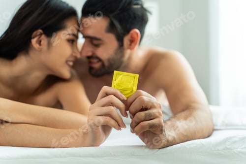 Preview: Attractive Caucasian young man and Asian woman holding condom together.