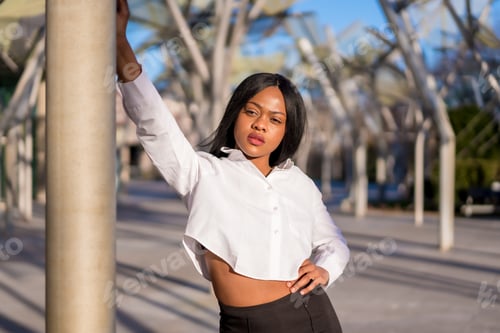 Preview: Young African woman in white clothes in the city at sunset, doing a fashion posing