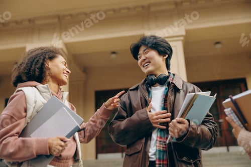 Preview: Young students talking and laughing together outdoor standing near campus and holding books