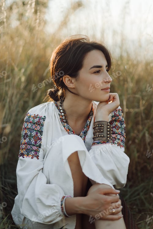 Preview: Young woman in traditional national embroidered shirt and skirt on nature at sunset.