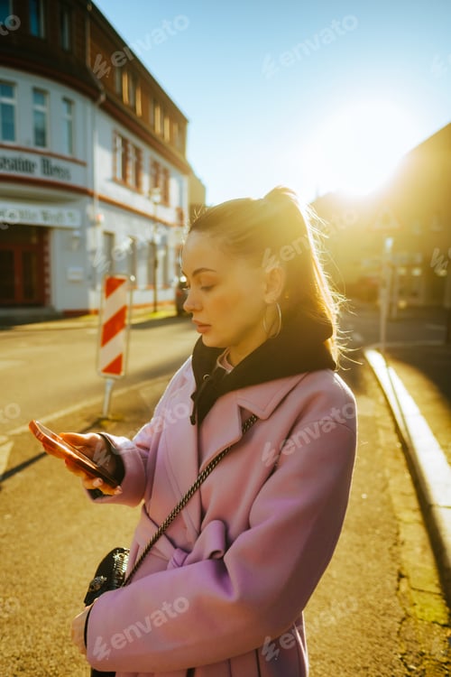 Preview: Young caucasian woman using mobile phone while walking on a city street.