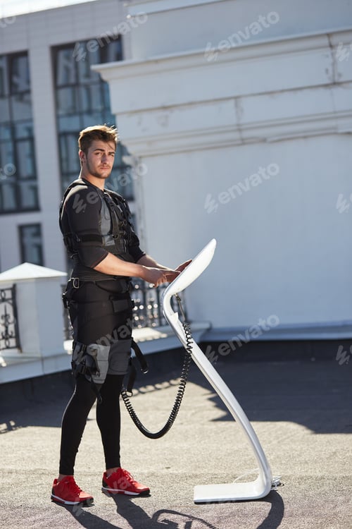 Preview: slim handsome man is looking at the camera while standing near the EMS device