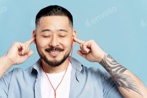 Preview: Attractive Korean man listenng music in headphones, eyes closed isolated on blue background