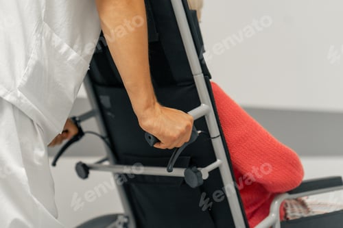 Vorschau: Nahaufnahme einer modernen Klinik in einem weißen Korridor, eine ältere Frau in einem korallenroten Pullover im Rollstuhl