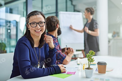 Preview: Portrait of a young businesswoman sitting in a meeting with colleagues in the background