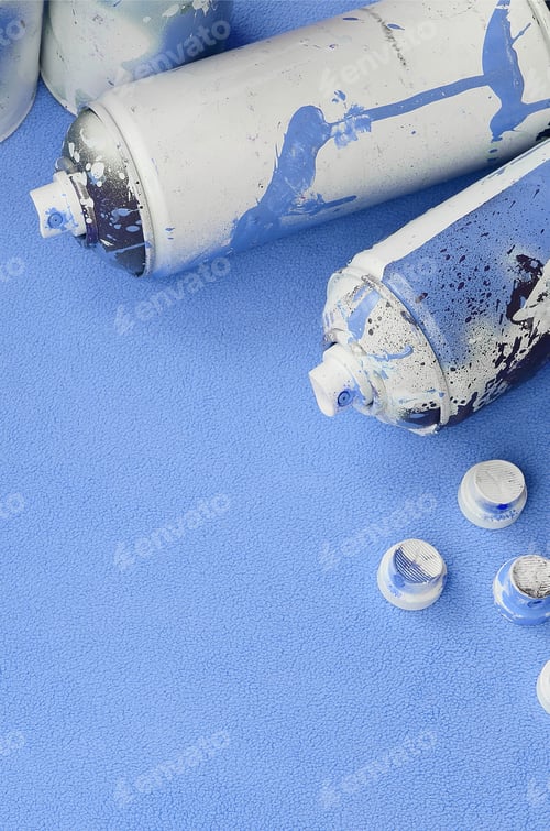 Preview: Some used blue aerosol spray cans and nozzles with paint drips lies on a blanket