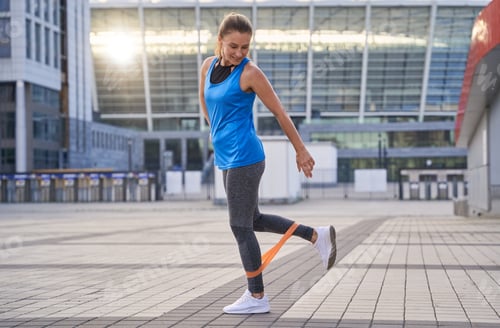 Preview: Full length shot of active sporty woman in sportswear warming up using resistance band while