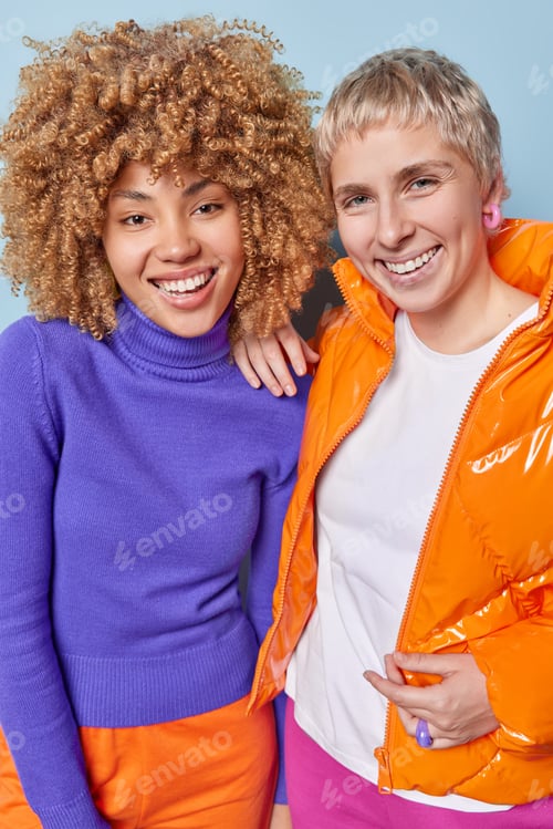 Preview: Vertical shot of cheerful young women dressed in fashionable clothes have fun together stand closely