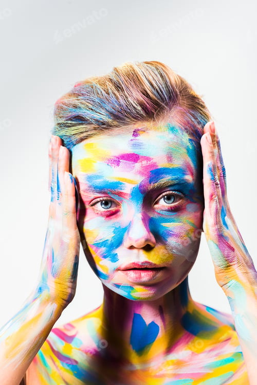 Preview: attractive girl with colorful bright body art touching head and looking at camera isolated on white