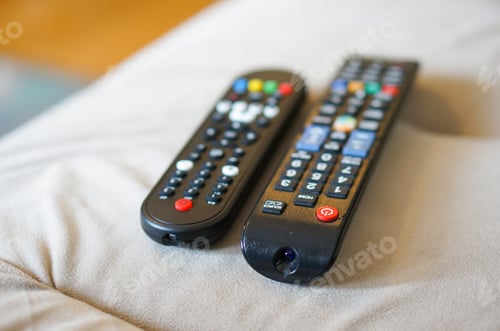 Preview: Selective focus shot of two black plastic television remotes on a sofa