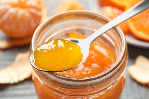 Preview: Teaspoon with tasty tangerine jam over jar, closeup