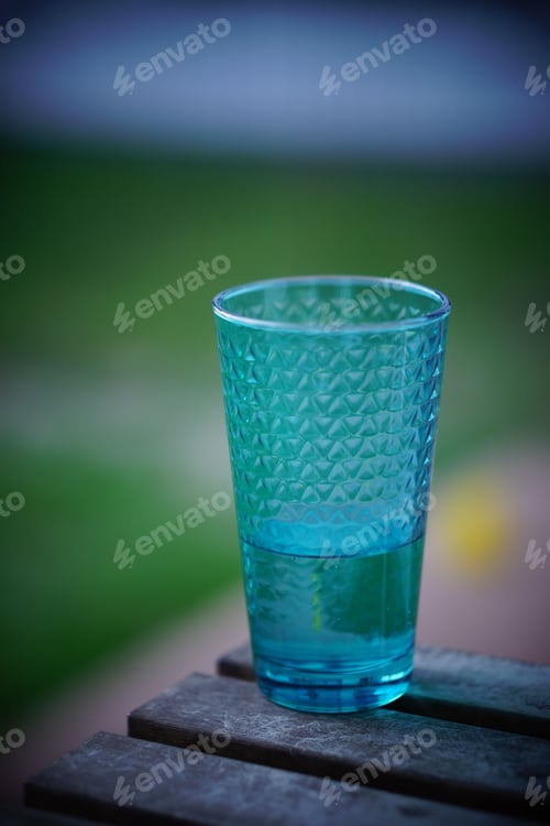 Preview: Blue glass of water is resting on a rustic bench table outdoors.