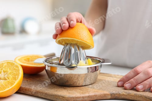 Preview: Making juice. Woman with orange using juicer at table indoors, closeup