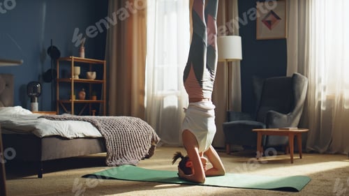 Preview: Strong girl maintaining headstand at home mat. Flexible woman training balance